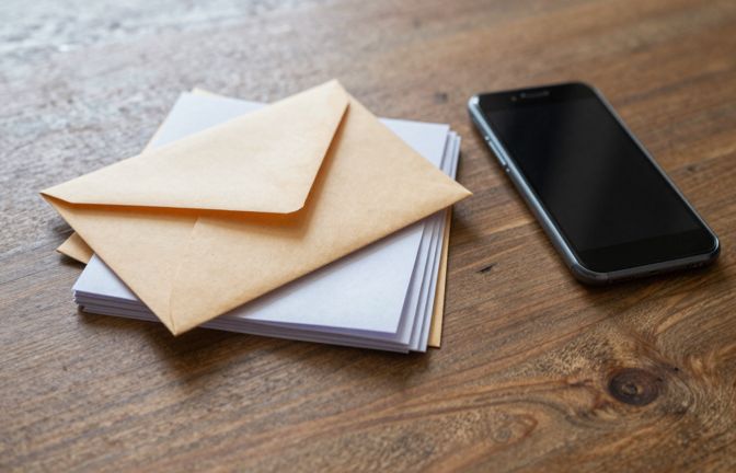 A small stack of opened paper envelopes and folded letters beside a smartphone lying face down on a timber desk